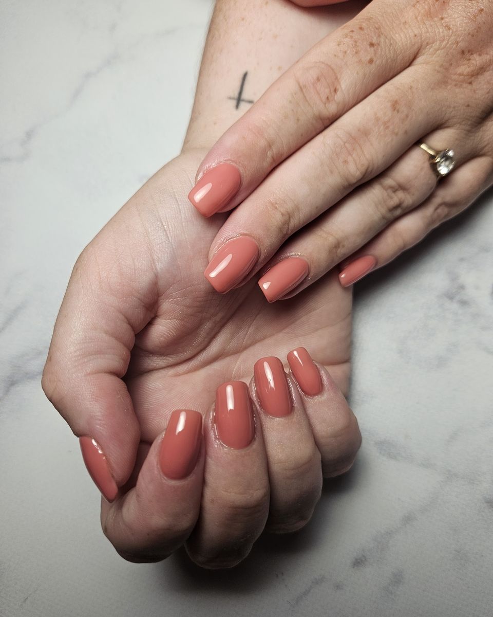 Korte nagels in een warme terracotta tint op een marmeren tafel