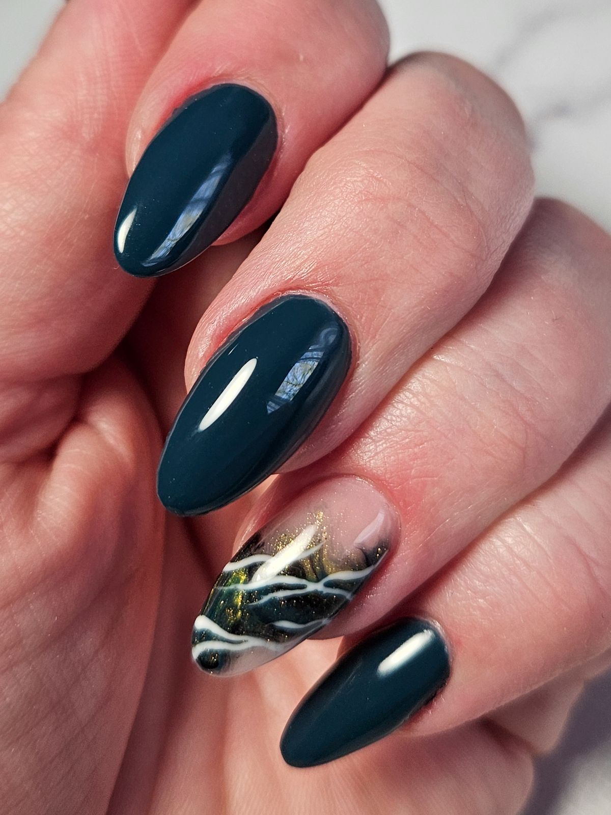 Donker petrolblauwe amandelnagels met een accentnagel met gouden adertjes