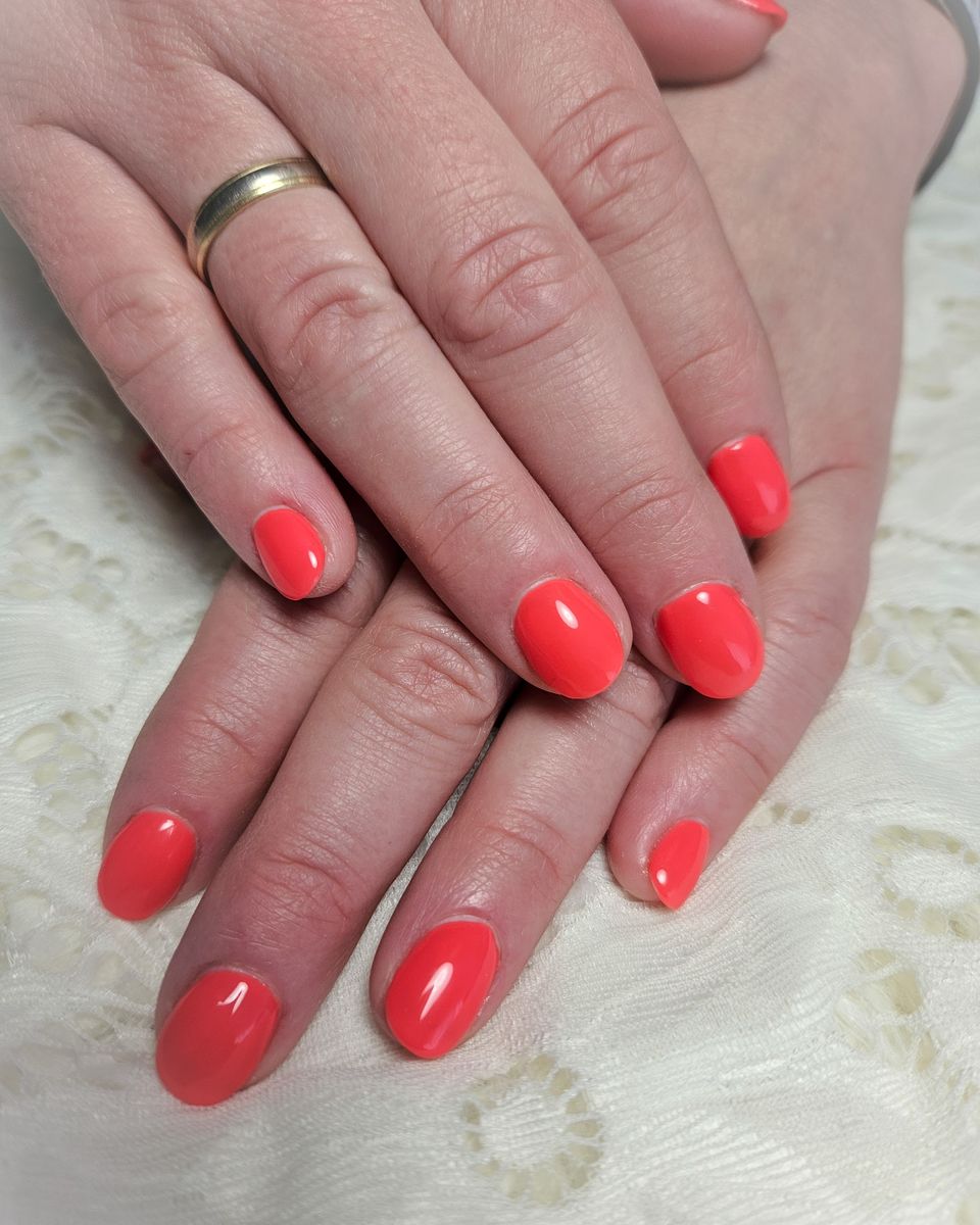 Korte koraalrode nagels op een wit kanten kleed
