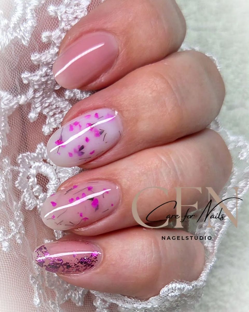 Roze nagels met gedroogde bloemetjes naast wit kant